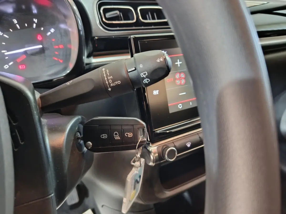 Détail intérieur du volant et du commodo de la Citroën C3 gris foncé, avec écran tactile et clé insérée.