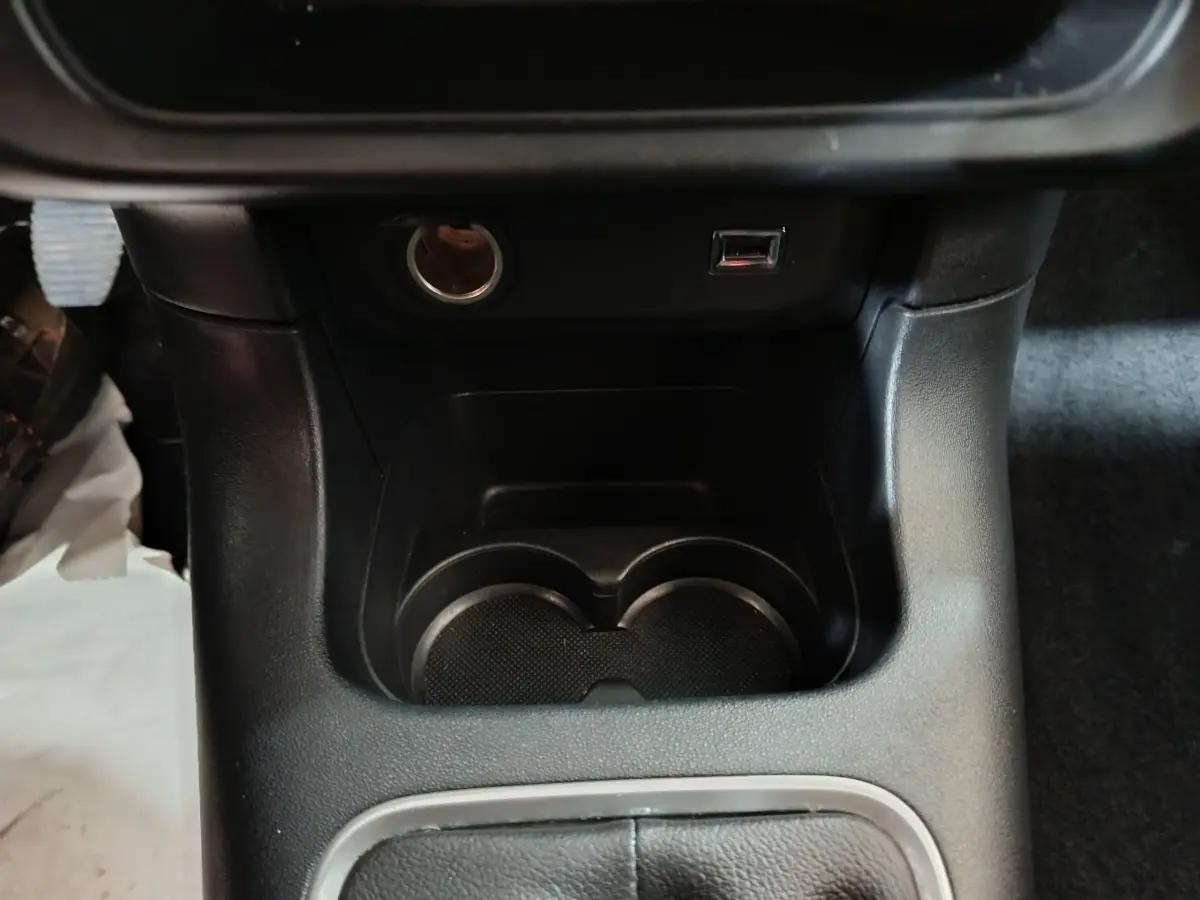Gros plan intérieur sur la console centrale noire avec prise 12V, port USB et porte-gobelets de la Citroën C3 2024.