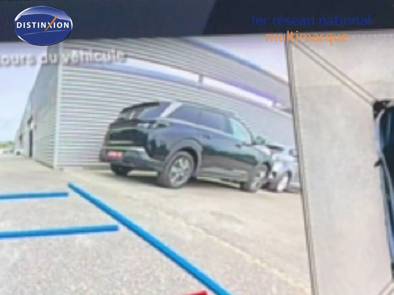 Vue 3/4 arrière d’un Peugeot 408 Hybrid 145ch GT noir métal garé devant un bâtiment industriel.