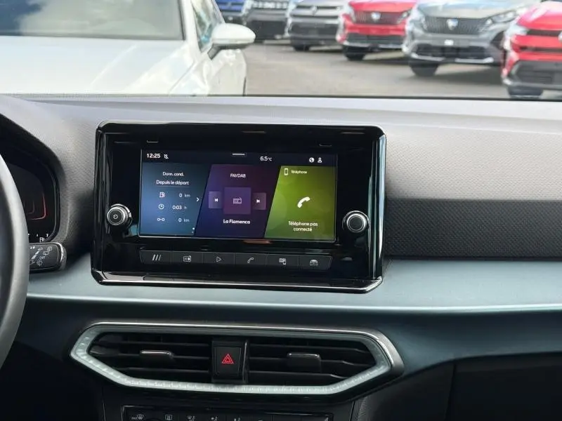 Vue rapprochée de l’écran tactile central du tableau de bord du SEAT Arona 2025, avec commandes et aérateurs visibles.