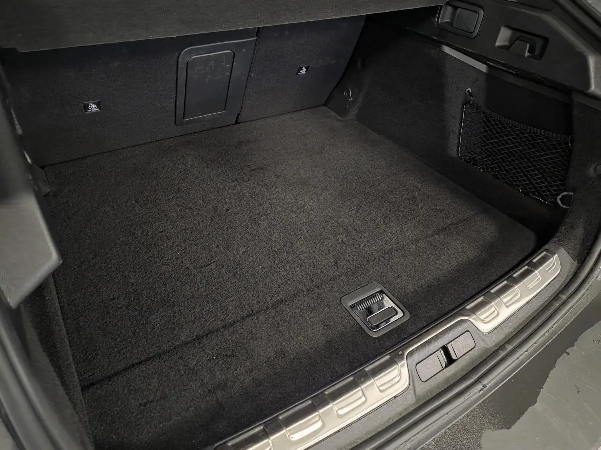 Coffre spacieux et propre du hayon arrière d'une Peugeot 408 gris, avec tapis noir et filet de rangement latéral.