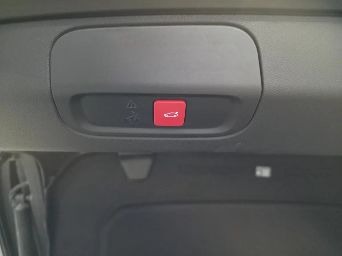 Bouton rouge d'ouverture électrique du hayon sur la partie intérieure du coffre d'une Peugeot 408 gris Selenium.