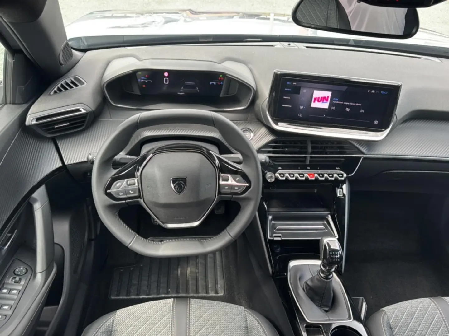 Vue intérieure frontale du tableau de bord et volant noir du Peugeot 2008 1.2 100 allure avec écran tactile et levier de vitesse manuel.