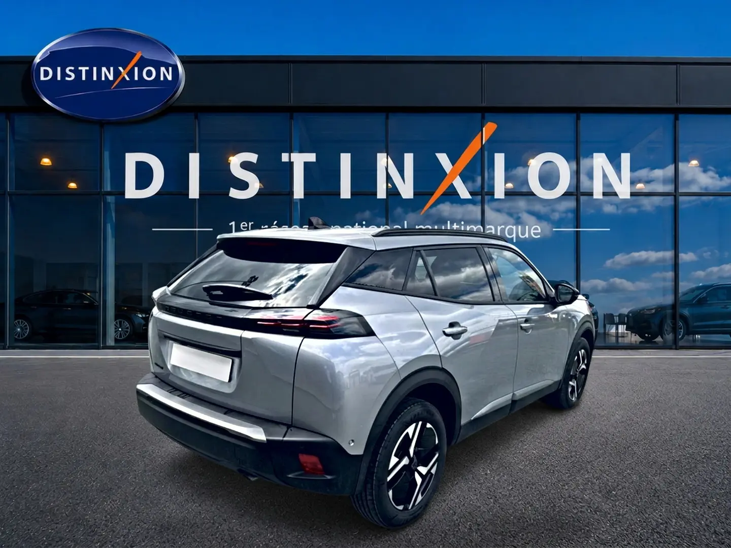 Peugeot 2008 gris artense en 3/4 arrière droit, avec jantes alu et feux arrière LED visibles devant showroom Distinxion.