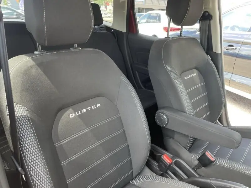Gros plan sur les sièges avant noirs du Dacia Duster TCE 150 Prestige 4x2 rouge métal, avec accoudoir côté droit visible.