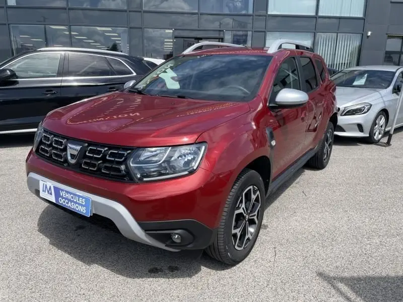 Dacia Duster rouge métal vu en 3/4 avant droit, avec calandre noire et jantes alliage distinctives.