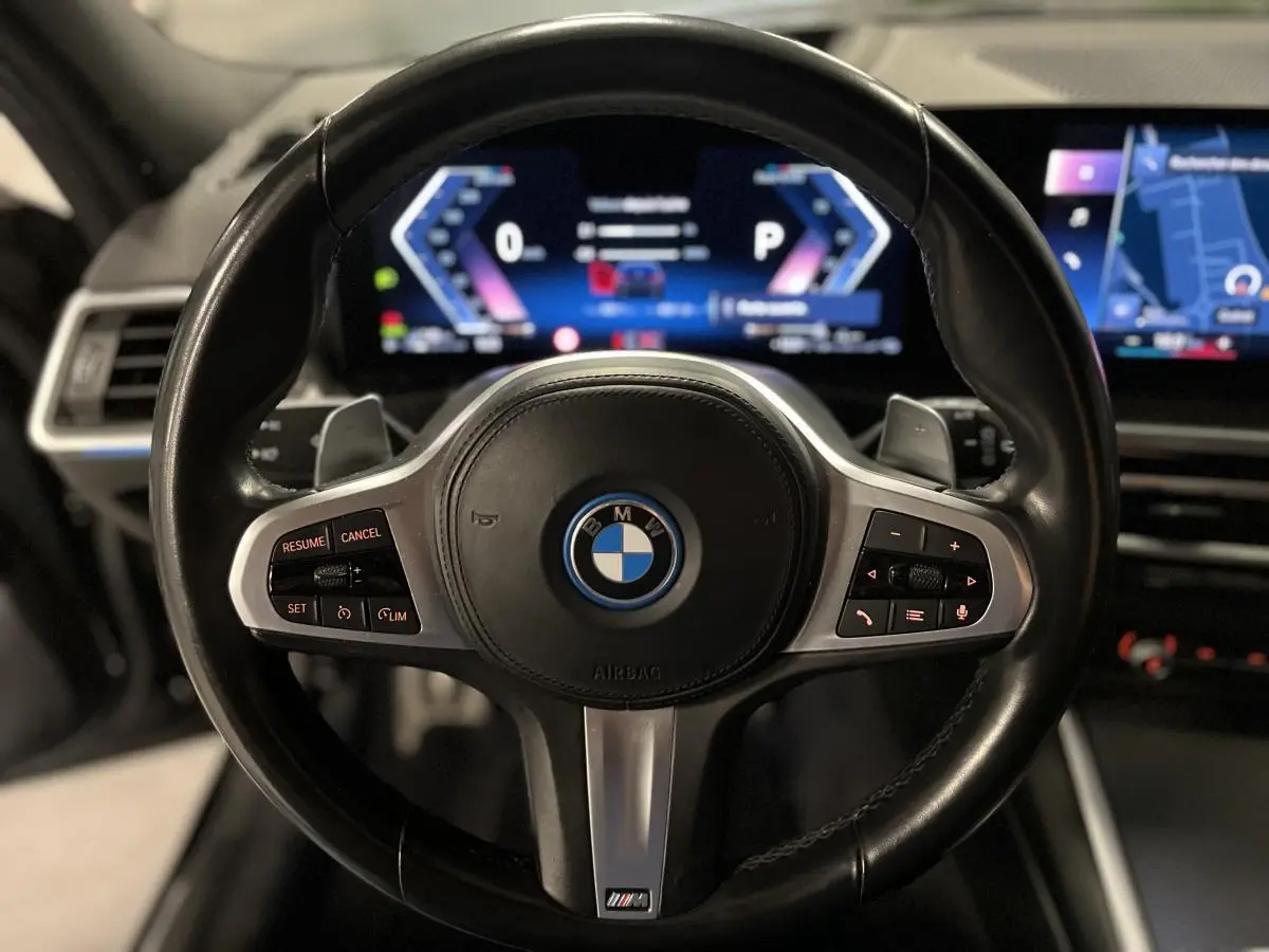 Volant M cuir noir BMW en gros plan avec tableau de bord numérique et écran de navigation en arrière-plan.