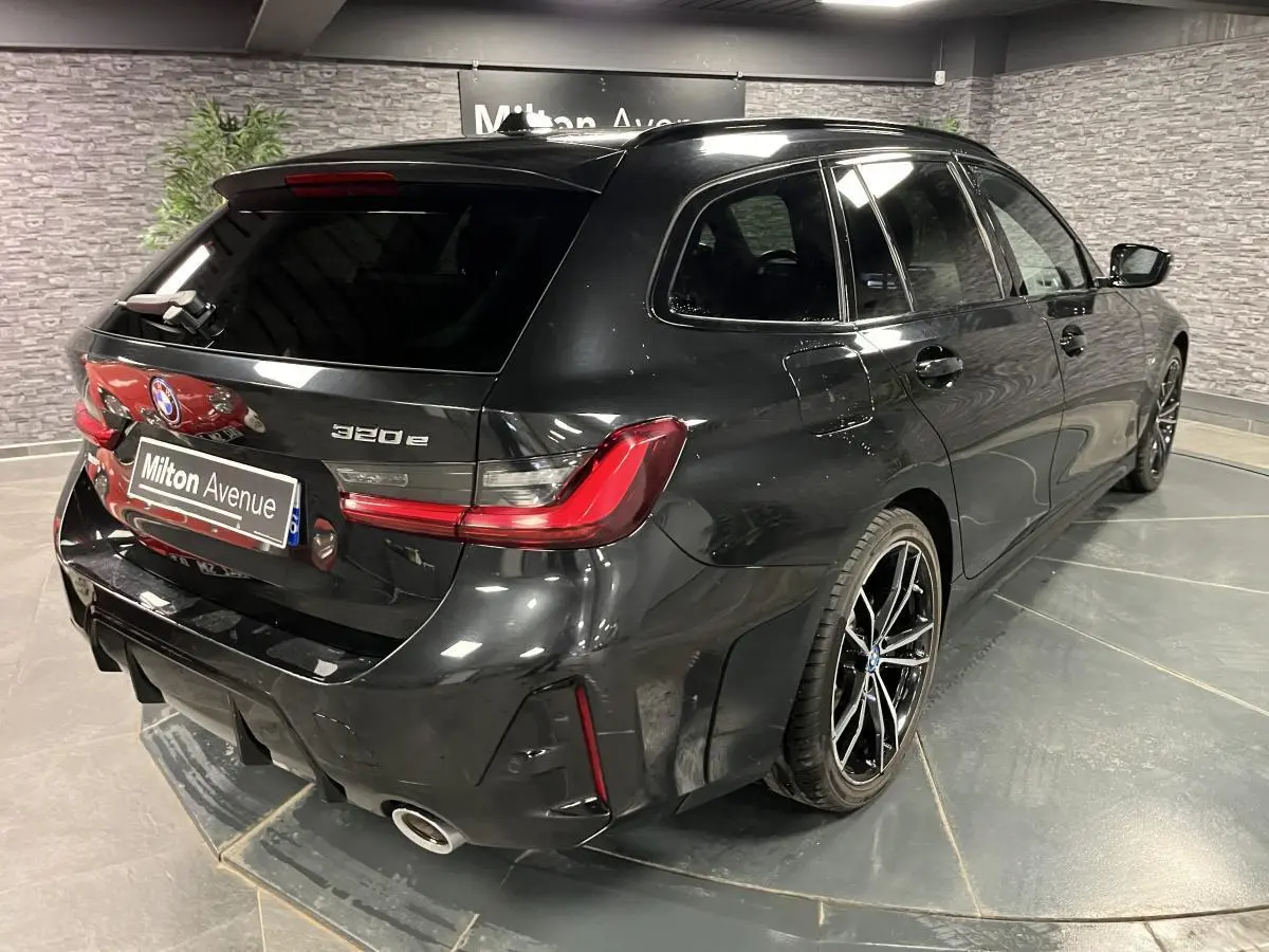 BMW Série 3 320e Touring noire vue 3/4 arrière droit avec jantes M sport bicolores et feux LED distinctifs.