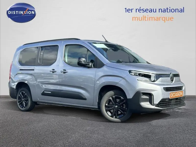 Vue 3/4 avant droite du Citroën Berlingo XL gris Artense avec jantes noires et barres de toit visibles.