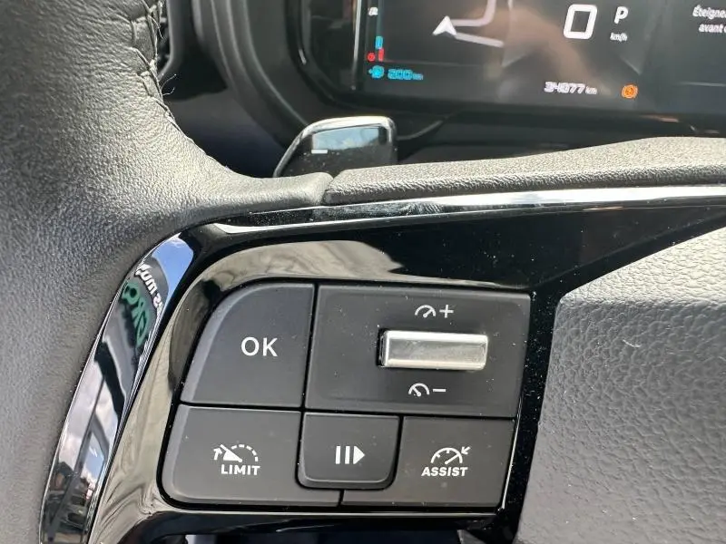 Gros plan sur les commandes du volant cuir noir du Citroën Berlingo gris Artense, avec affichage numérique en arrière-plan.