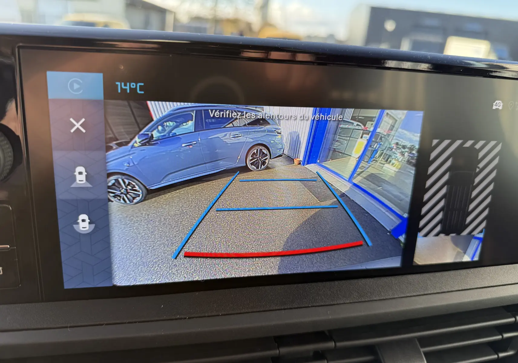 Vue caméra de recul montrant une voiture grise garée côté droit devant une baie vitrée, affichage sur écran intérieur.