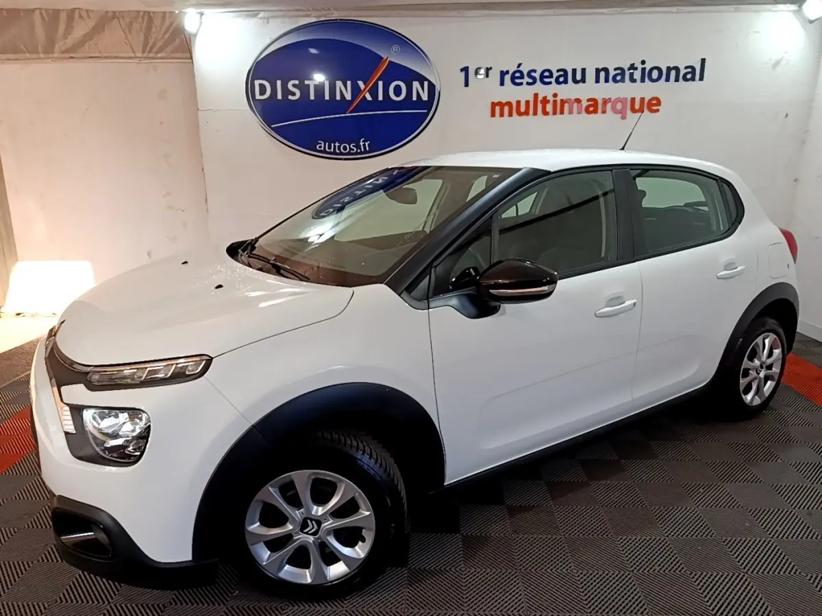 Vue 3/4 avant droit d'une Citroën C3 blanche avec protections noires et jantes alliage en showroom.