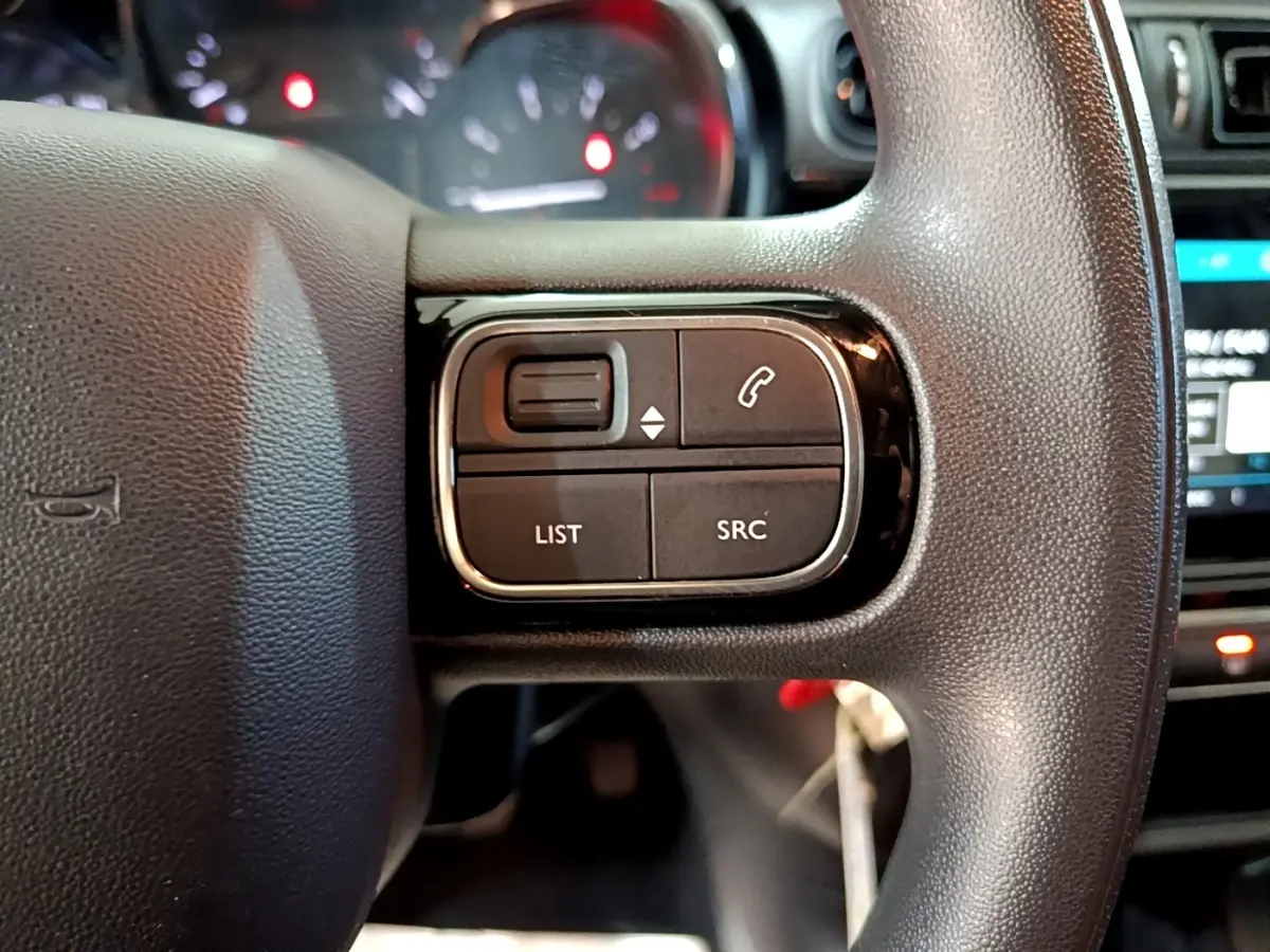 Gros plan sur les commandes du volant à droite d’une Citroën C3 blanche, avec boutons de téléphone et liste.
