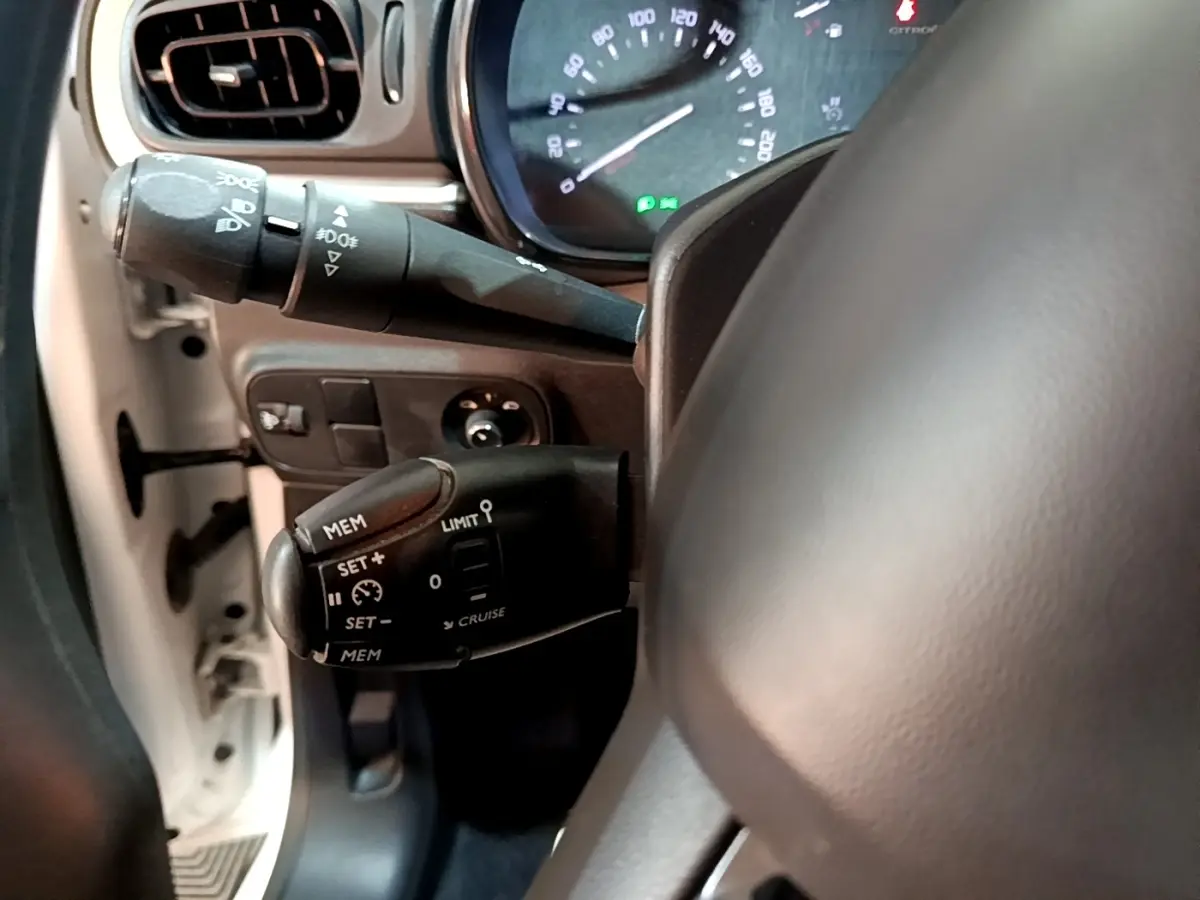 Vue rapprochée du commodo de régulateur de vitesse côté gauche du volant dans une Citroën C3 blanche de 2020.