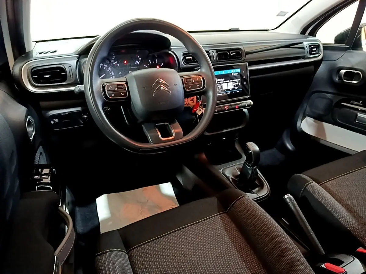 Vue intérieure de face du poste de conduite de la Citroën C3 blanche, avec volant multifonctions et écran tactile central.