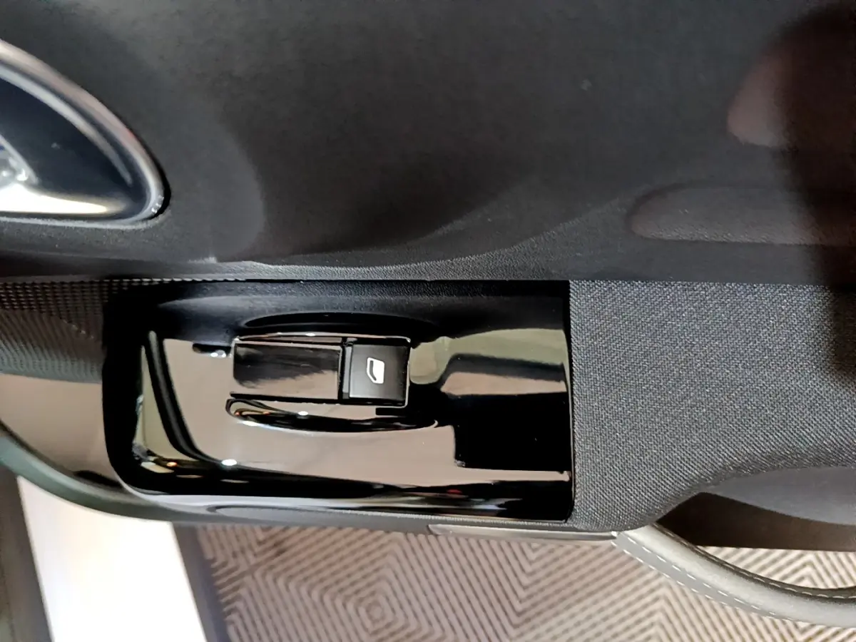 Bouton de commande de lève-vitre sur la portière côté conducteur d'une Citroën C3 blanche, vue rapprochée intérieure.