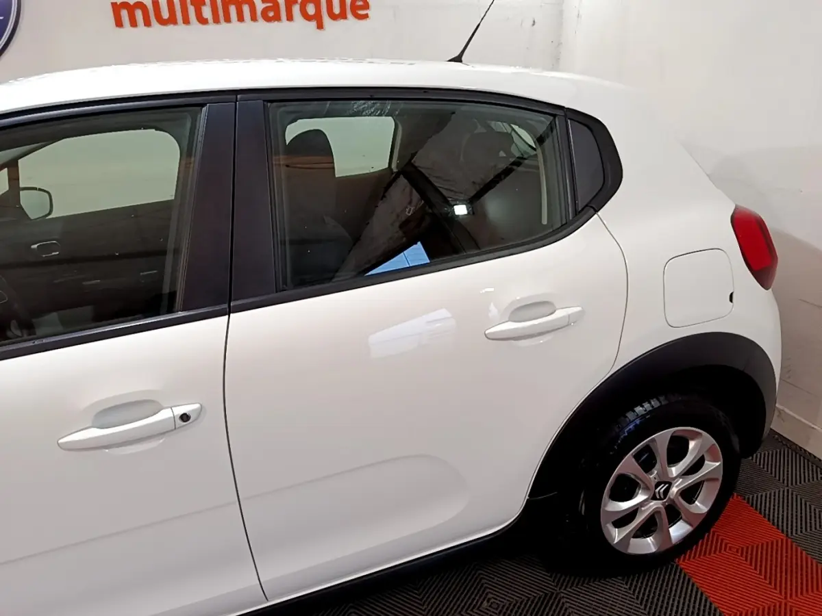 Vue latérale droite d'une Citroën C3 blanche avec poignées et rétroviseurs ton caisse, en intérieur showroom.