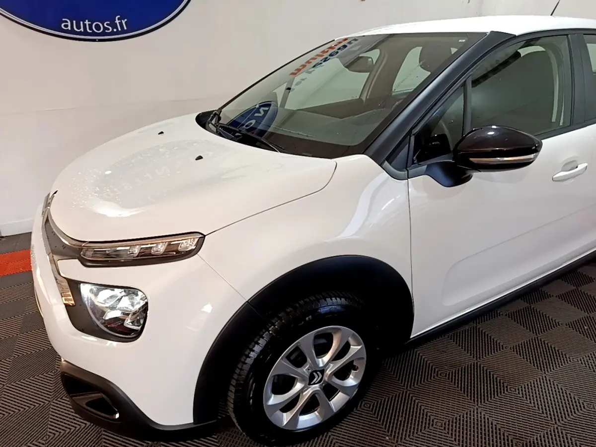 Vue 3/4 avant droit d'une Citroën C3 blanche avec rétroviseurs noirs et jantes alliage argentées.