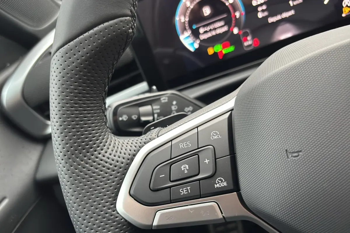 Gros plan sur le volant cuir perforé à gauche du Volkswagen T-Roc 2026 avec commandes multifonctions et tableau de bord numérique flou.