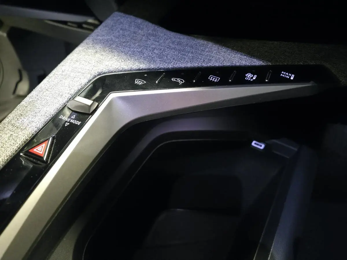 Gros plan sur la console centrale tissu gris chiné du Peugeot 3008 Hybrid 2025 avec commandes tactiles et prise USB-C.