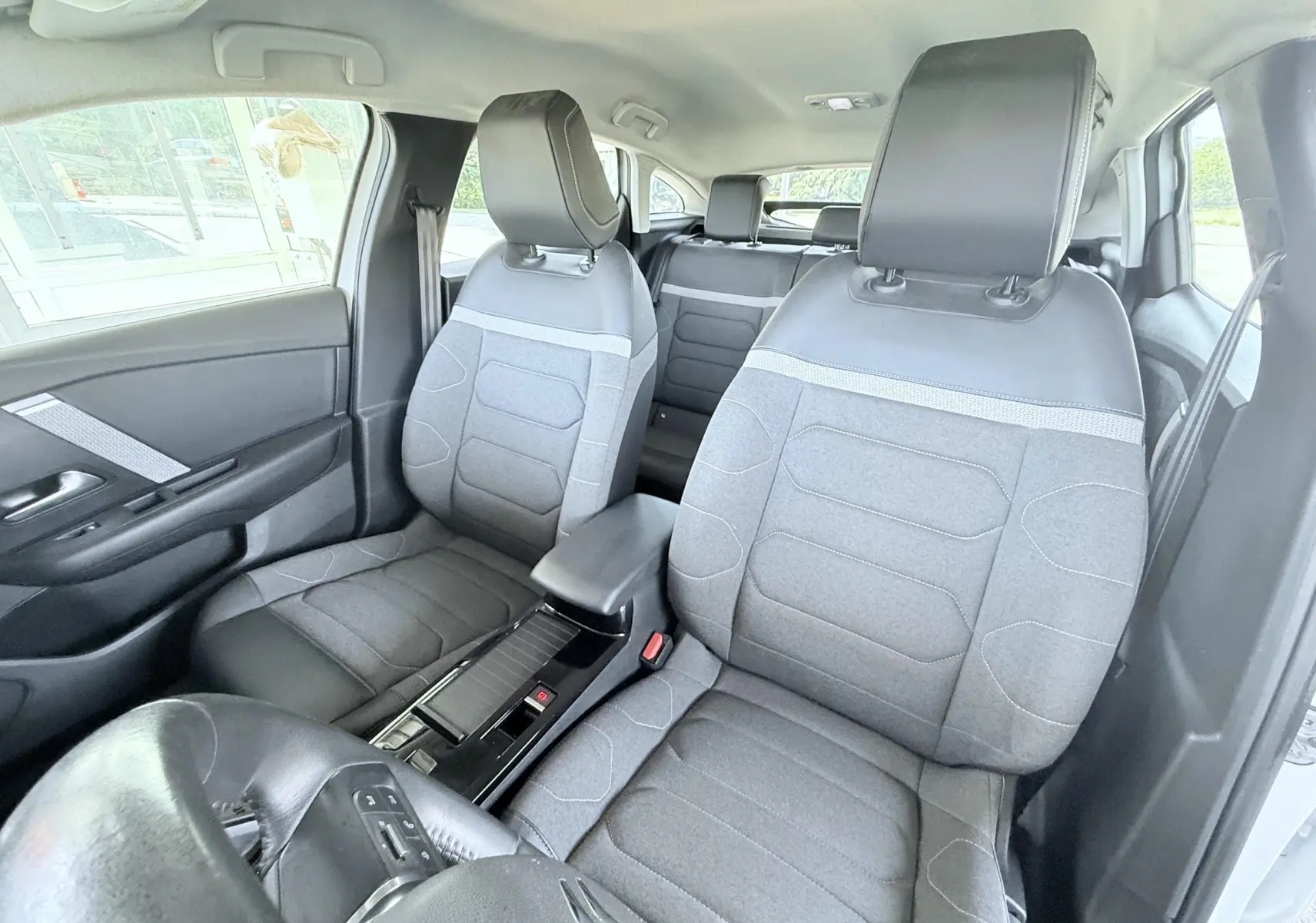 Vue intérieure avant de la Citroën C4 2023, sièges gris tissu avec appuie-têtes noirs et console centrale noire.