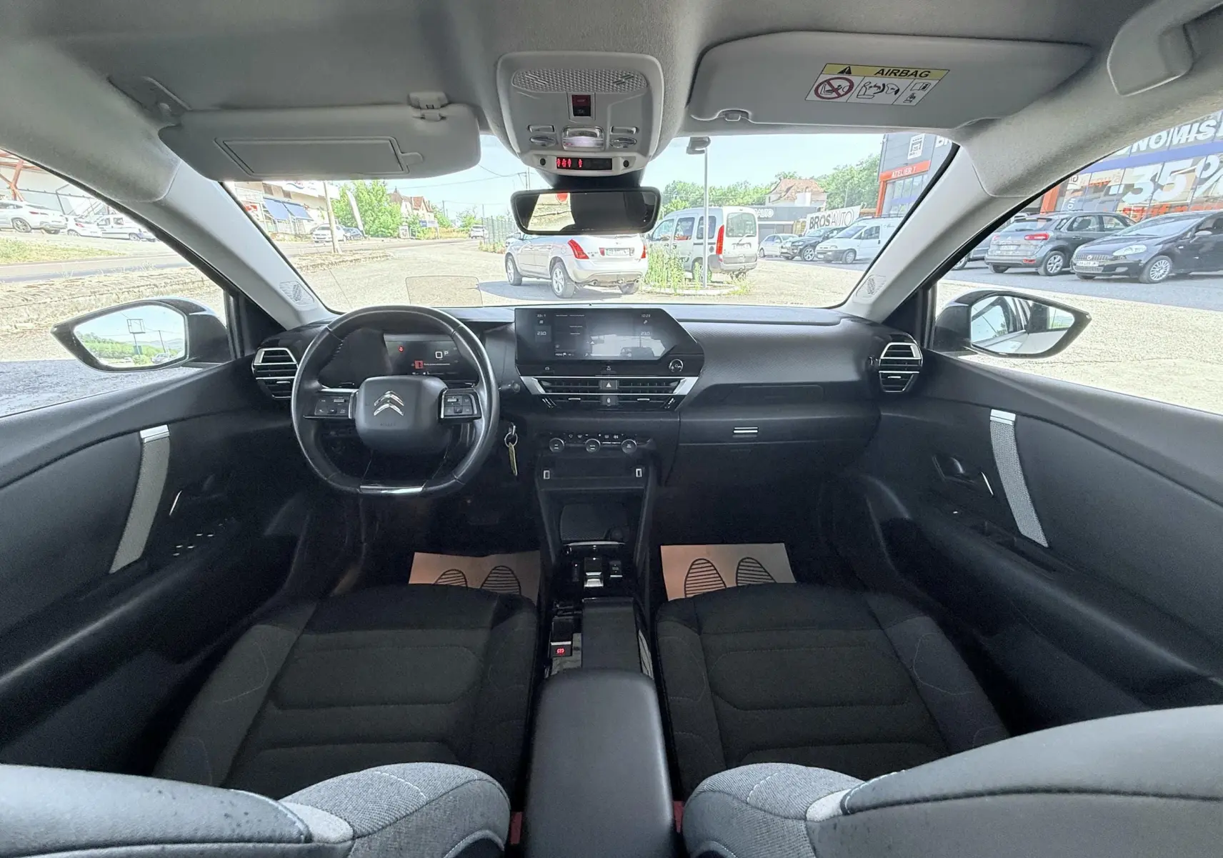 Vue intérieure avant de la Citroën C4 2023, tableau de bord noir avec écran tactile et sièges tissu gris foncé.