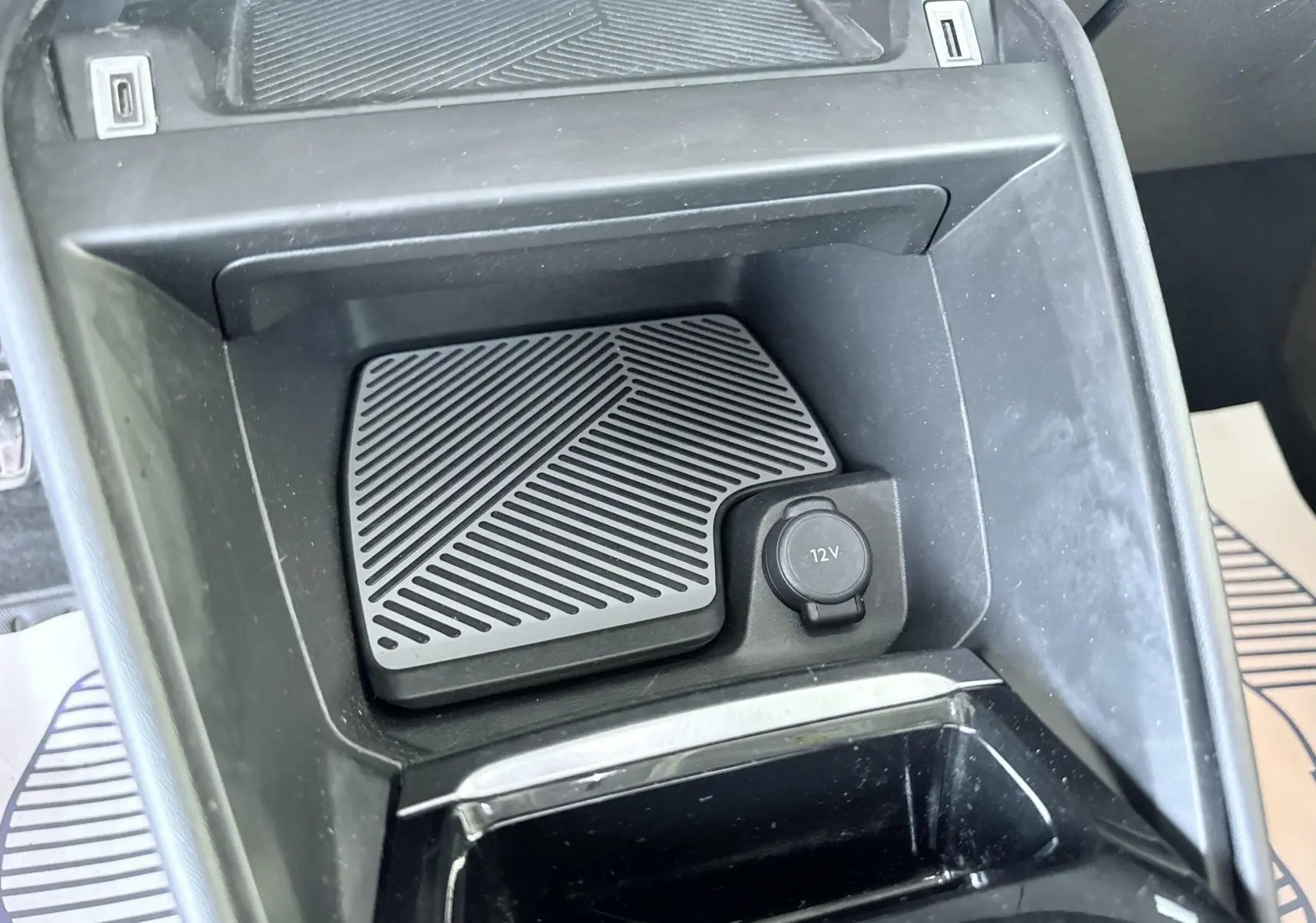 Gros plan sur la console centrale noire de la Citroën C4 2023, montrant une prise 12V et un espace de rangement.