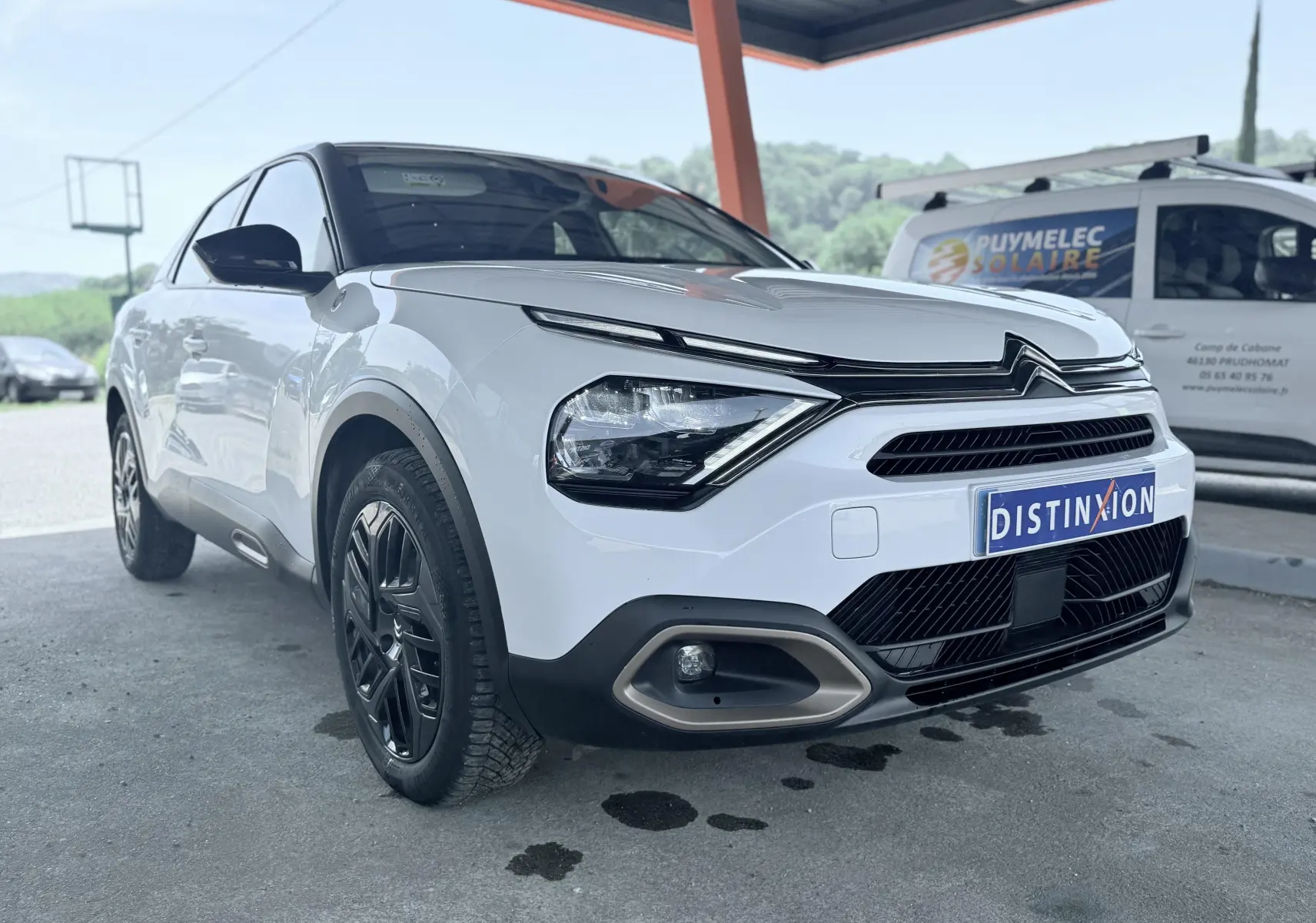 Vue 3/4 avant gauche d'une Citroën C4 blanche avec calandre distinctive et jantes noires sous abri.