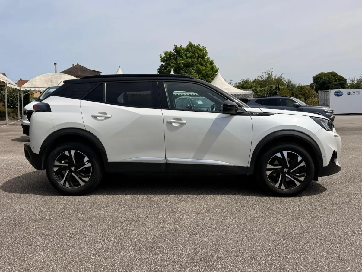 Profil droit d’un Peugeot 2008 blanc 2021 avec toit noir et jantes alliage noires, stationné en extérieur.