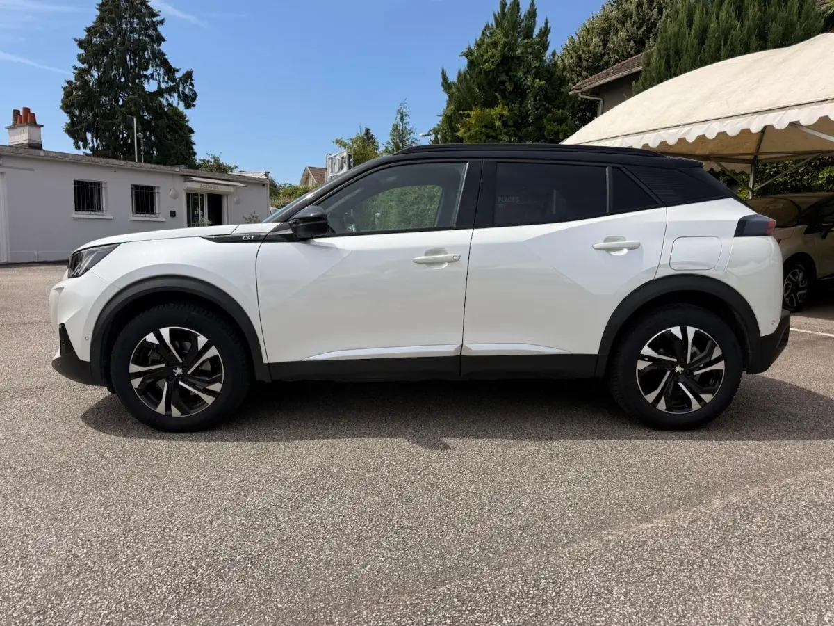 Vue de profil côté gauche d’un Peugeot 2008 blanc avec toit noir et jantes alliage noires, stationné en extérieur.
