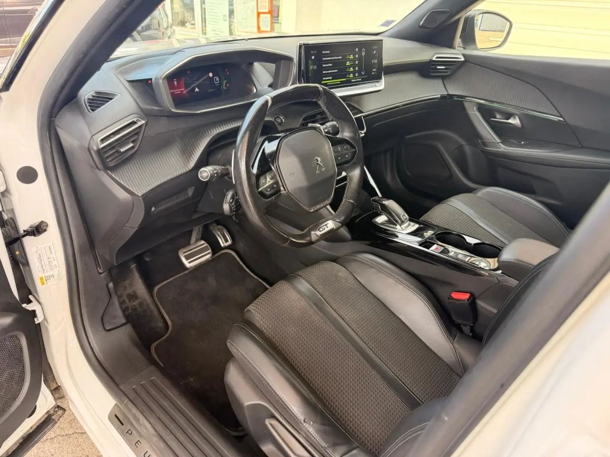 Vue intérieure côté conducteur du Peugeot 2008 blanc, mettant en valeur le volant GT, la sellerie tri-matière et l'écran tactile central.