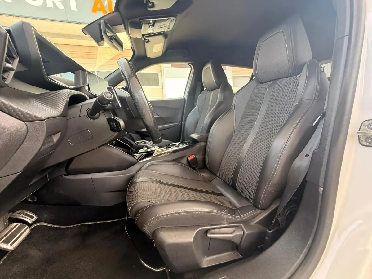 Vue intérieure côté conducteur du Peugeot 2008 blanc 2021, mettant en valeur les sièges sport en tissu et cuir noir.
