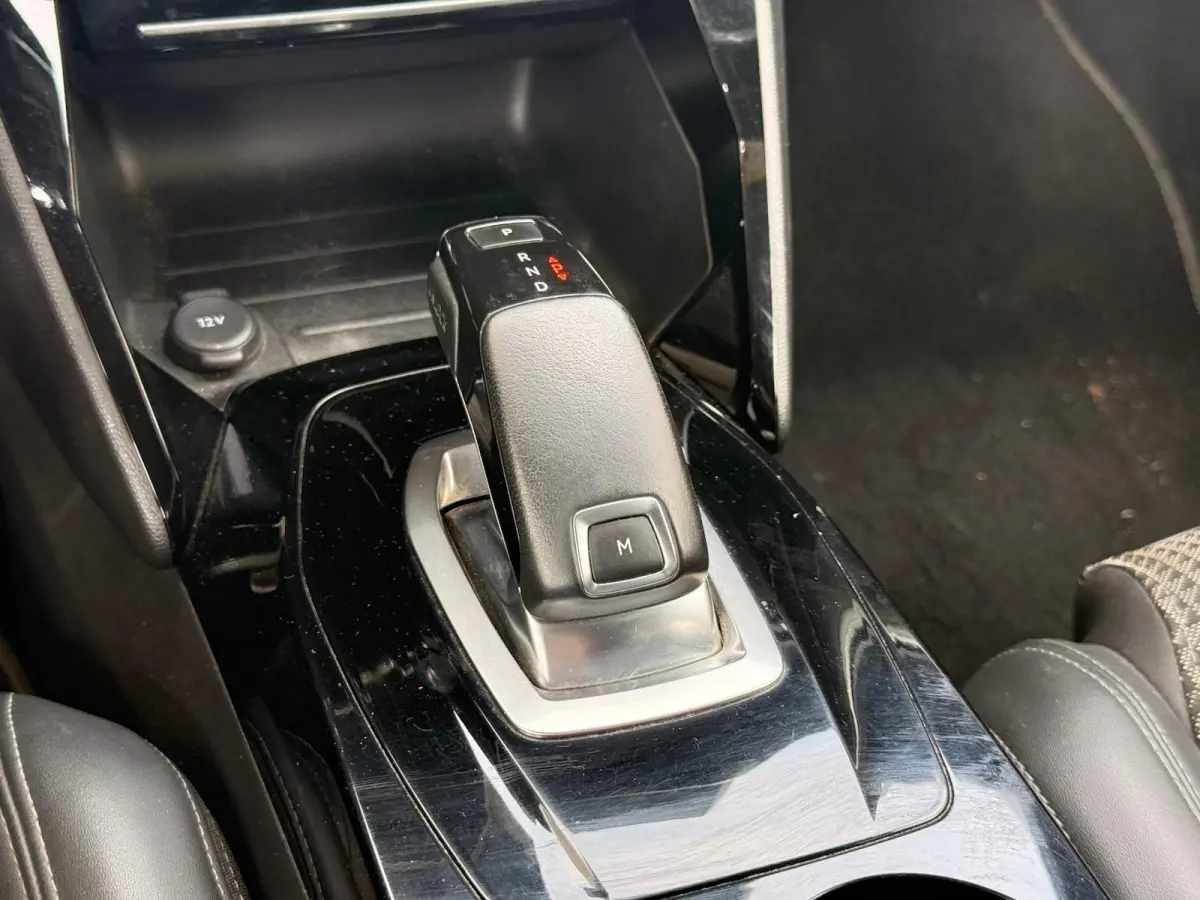 Gros plan sur la commande de boîte automatique noire au centre de la console d’une Peugeot 2008 blanche, intérieur sombre.