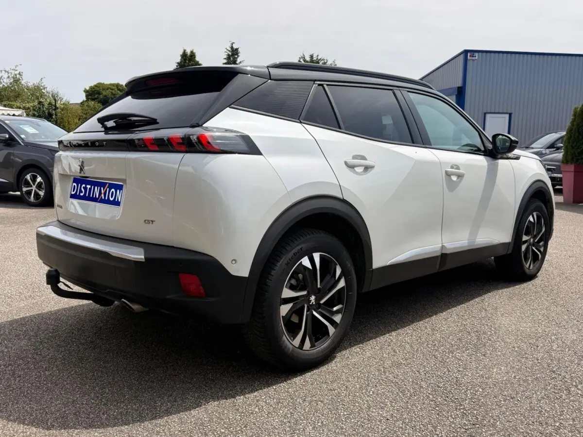 Vue 3/4 arrière droite d’un Peugeot 2008 blanc avec toit noir et jantes alliage distinctives, stationné en extérieur.