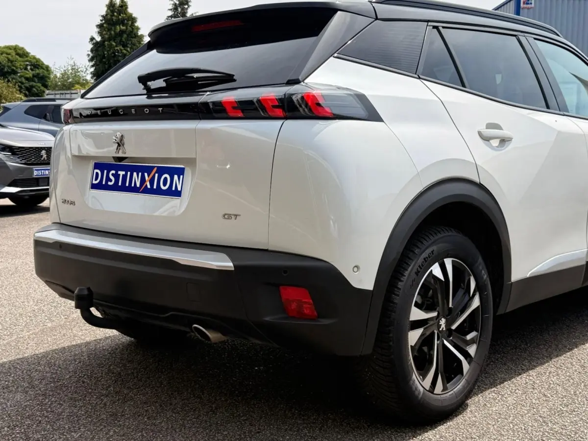 Vue 3/4 arrière droite du Peugeot 2008 blanc avec toit noir, feux arrière à LED et attelage visible.
