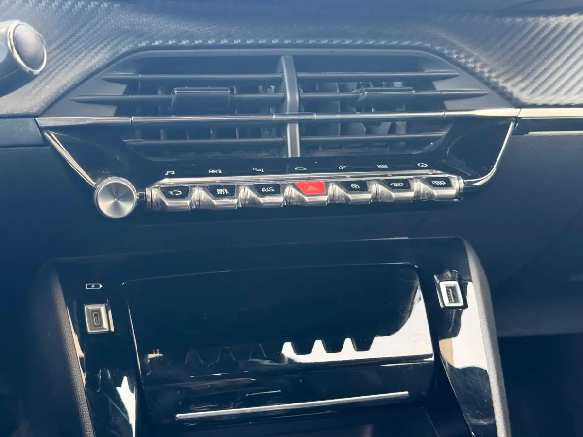Gros plan sur la console centrale noire brillante du Peugeot 2008 1.5 BlueHDi 130ch, avec commandes et prises USB visibles.