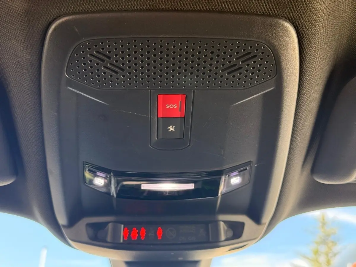 Vue en contre-plongée du plafonnier intérieur noir du Peugeot 2008 blanc, avec bouton SOS rouge et éclairage LED allumé.
