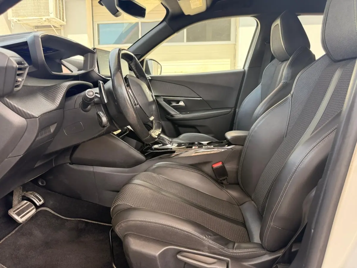 Vue intérieure côté conducteur du Peugeot 2008 blanc, mettant en valeur les sièges noirs en tri-matière avec surpiqûres et le volant cuir.