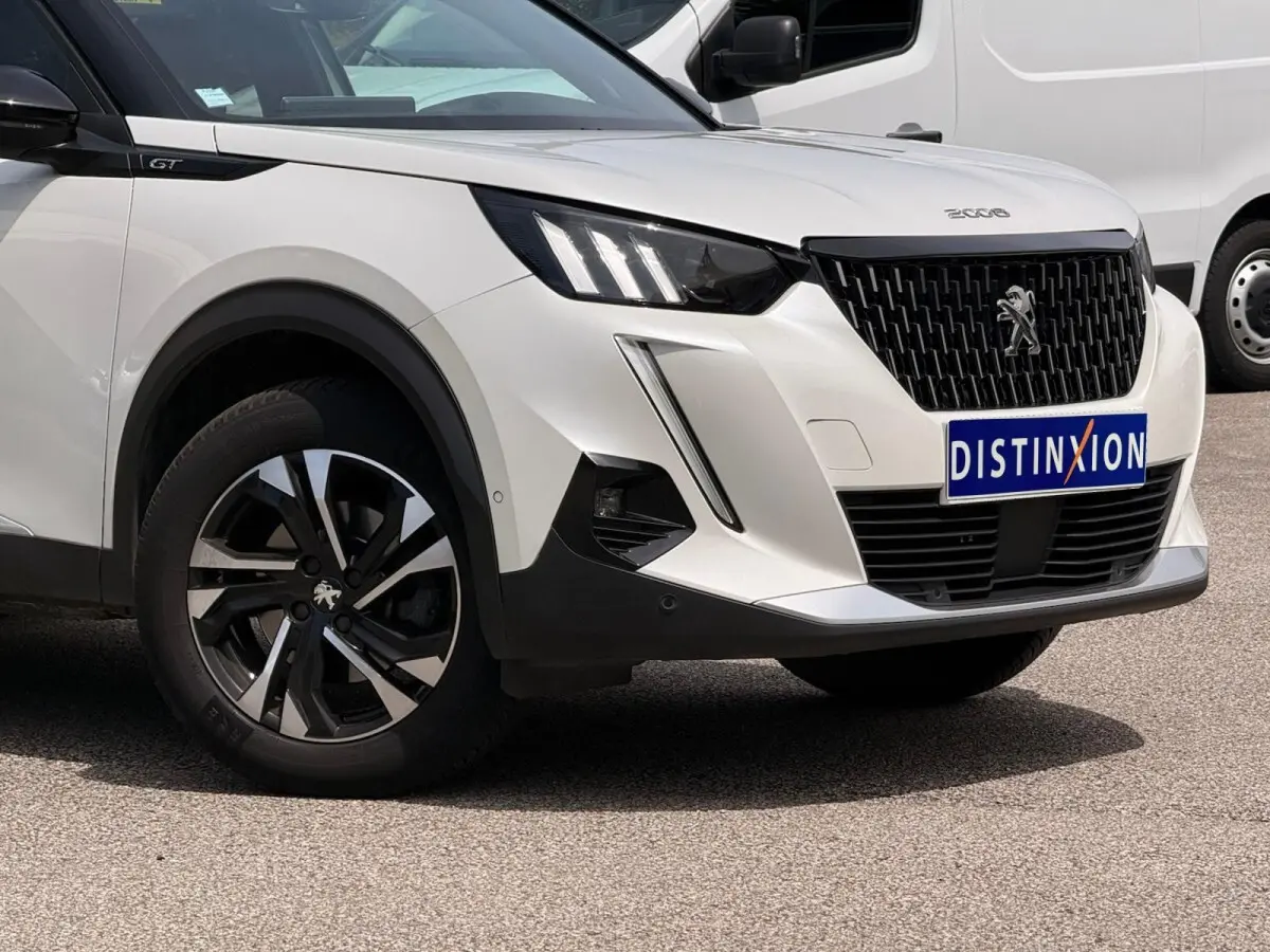 Vue 3/4 avant droit du Peugeot 2008 blanc avec calandre noire et jantes alliage bicolores.