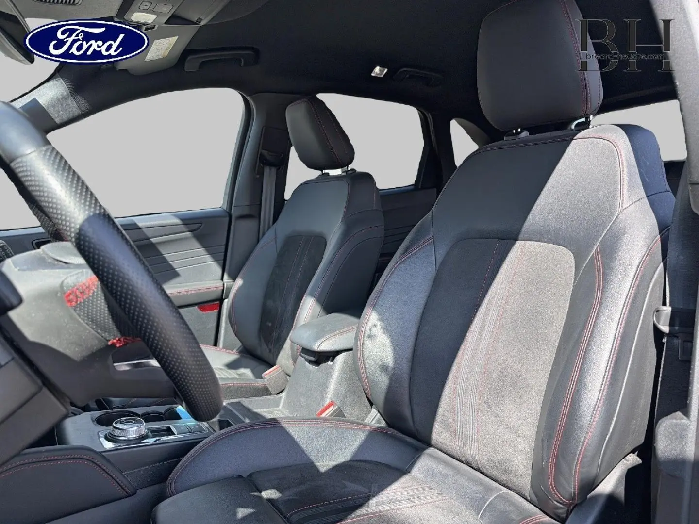 Vue intérieure côté conducteur du Ford Kuga 2024, sièges sport en suédine grise avec surpiqûres rouges visibles.