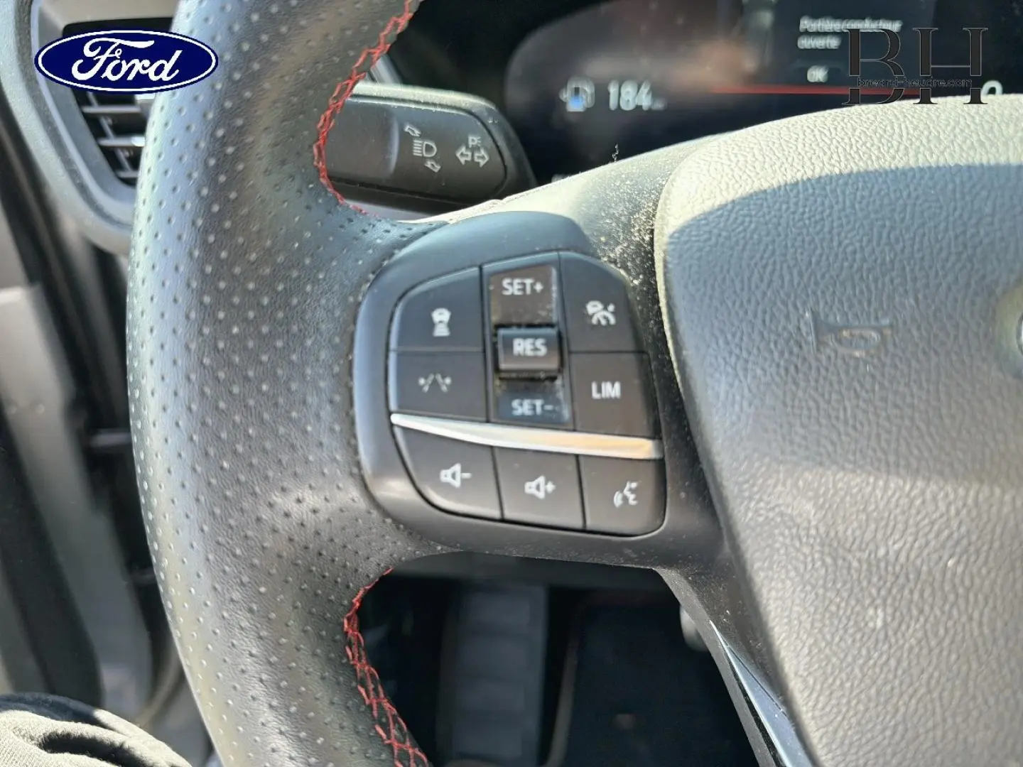 Gros plan sur le volant sport noir à surpiqûres rouges du Ford Kuga 2024 avec commandes intégrées.