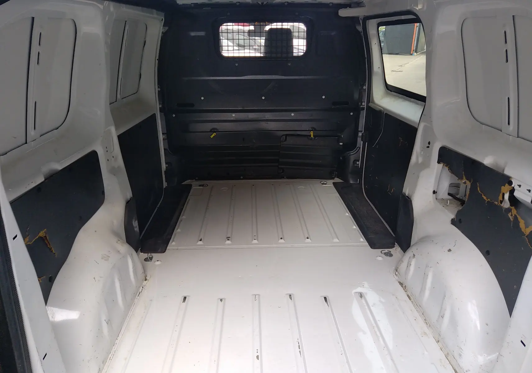 Vue intérieure arrière du fourgon Peugeot Expert blanc uni, montrant l'espace de chargement vide avec parois métalliques et grille de séparation noire.