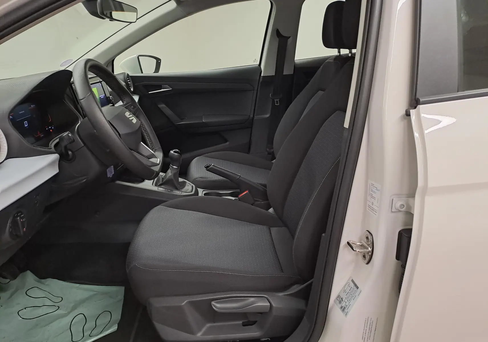 Intérieur côté conducteur d'une SEAT Ibiza blanc candy 2023, montrant sièges noirs et volant avec boîte manuelle.