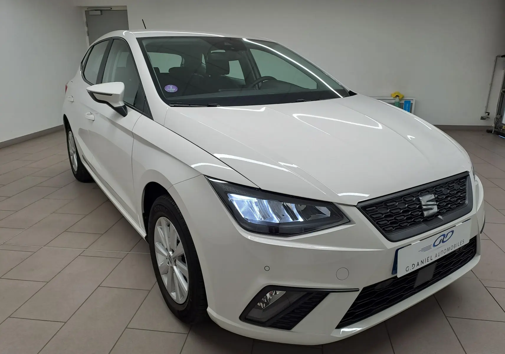 SEAT Ibiza blanc candy vue 3/4 avant droit, phares allumés et calandre noire avec logo central.