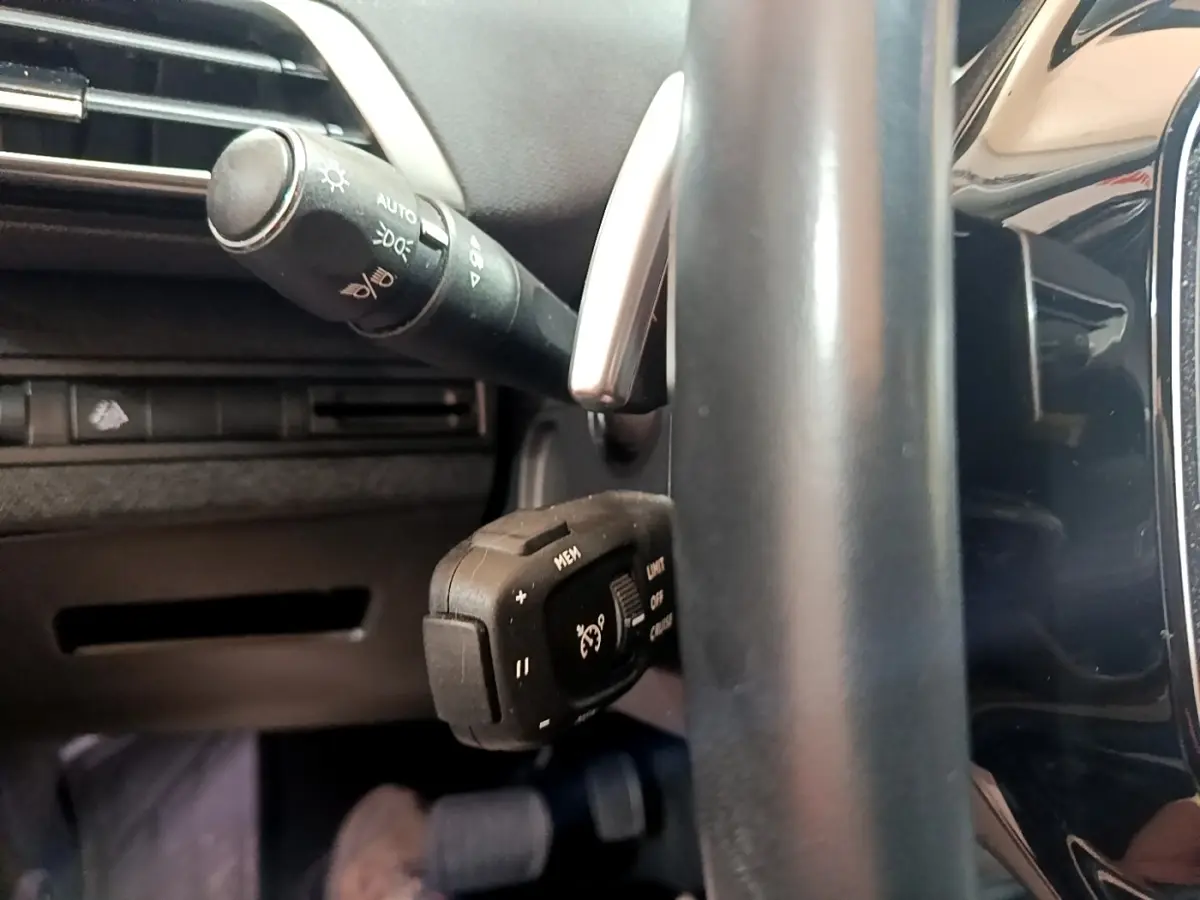 Gros plan sur la commande de régulateur de vitesse et levier d'éclairage côté gauche du volant cuir noir du Peugeot 3008 gris foncé.