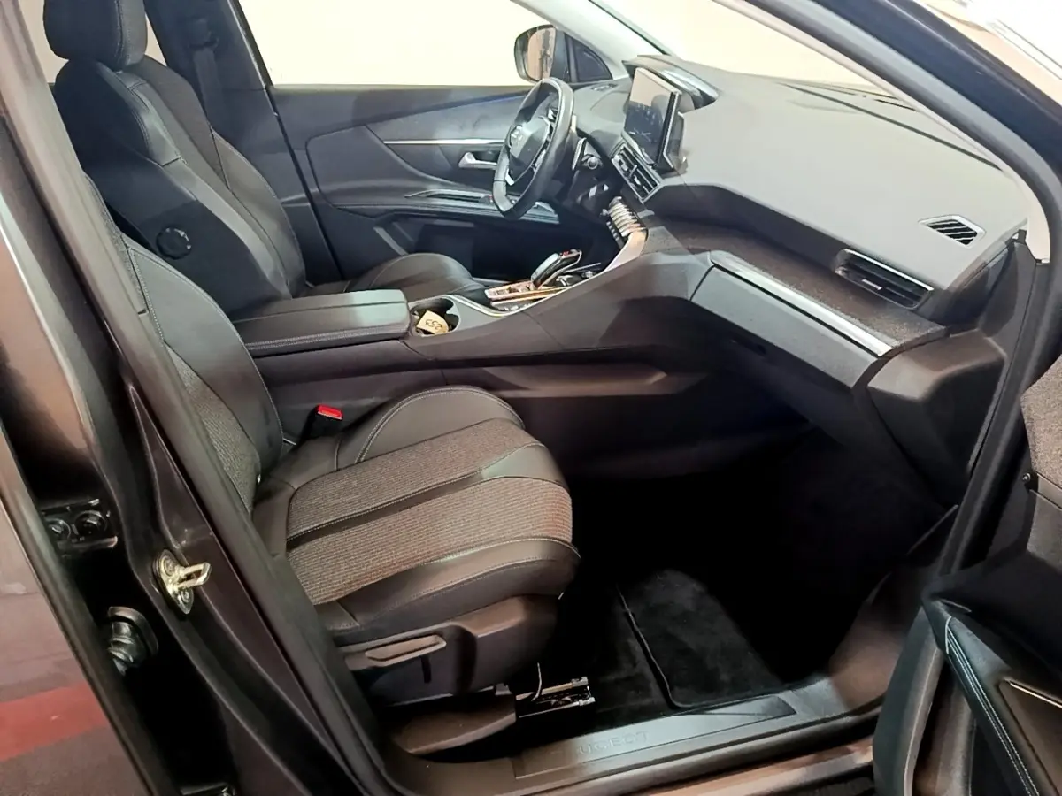 Intérieur avant droit du Peugeot 3008 2022 gris foncé, sièges tissu et cuir, tableau de bord avec écran tactile central.