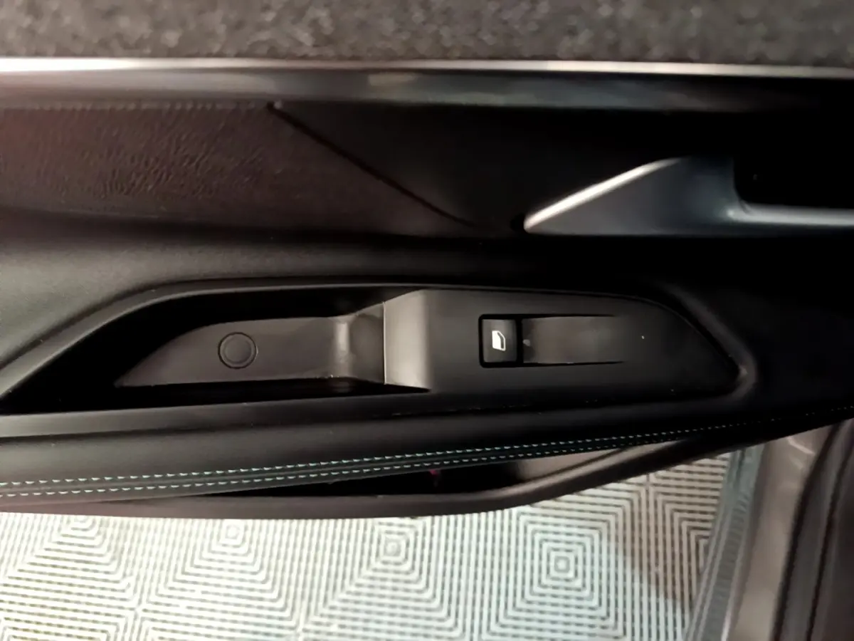 Gros plan sur la commande de lève-vitre côté gauche avec surpiqûres bleues sur la garniture intérieure noire du Peugeot 3008 gris foncé.