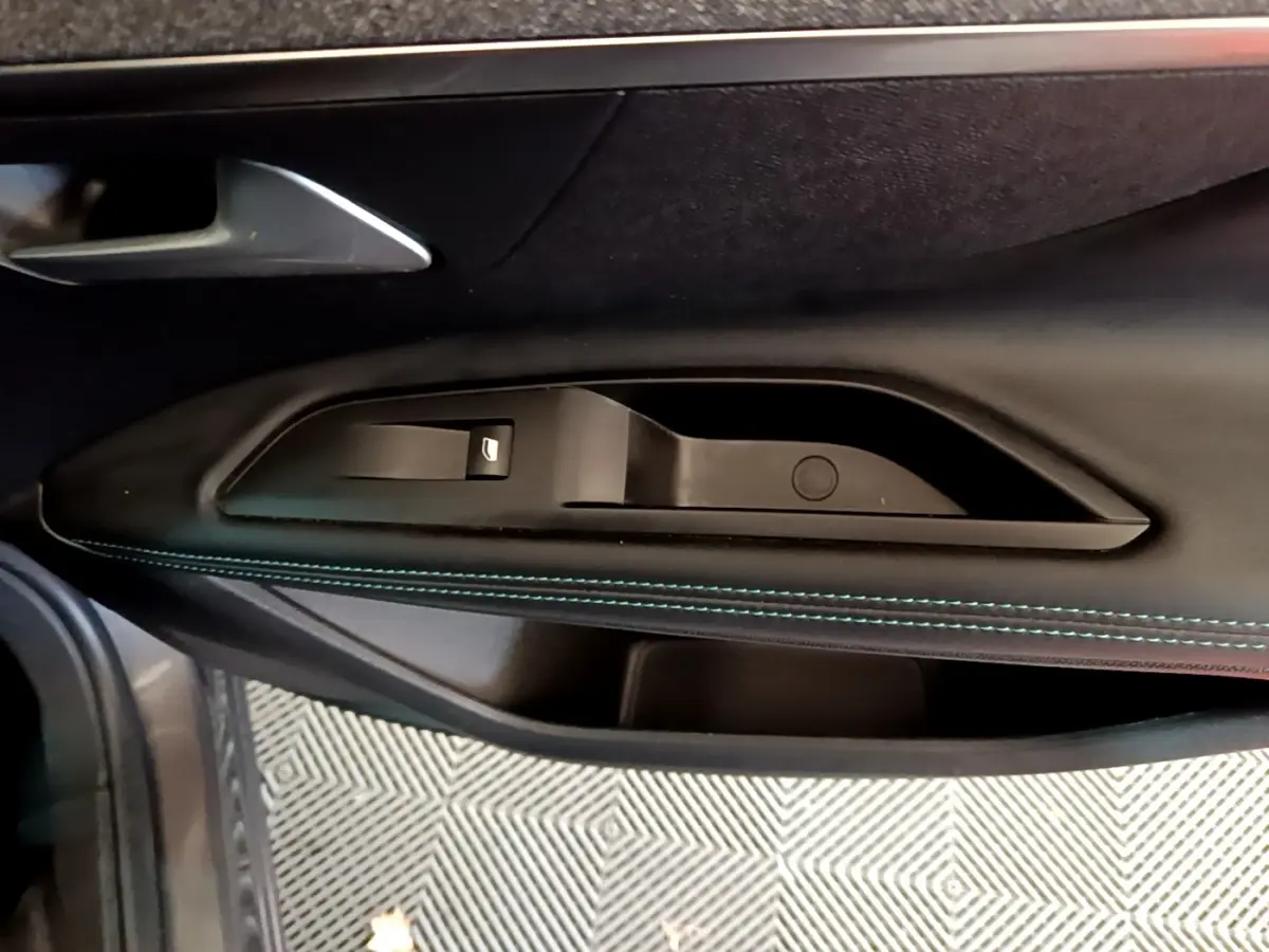 Détail de la porte côté gauche du Peugeot 3008 gris foncé, avec bouton de lève-vitre et surpiqûres bleues.