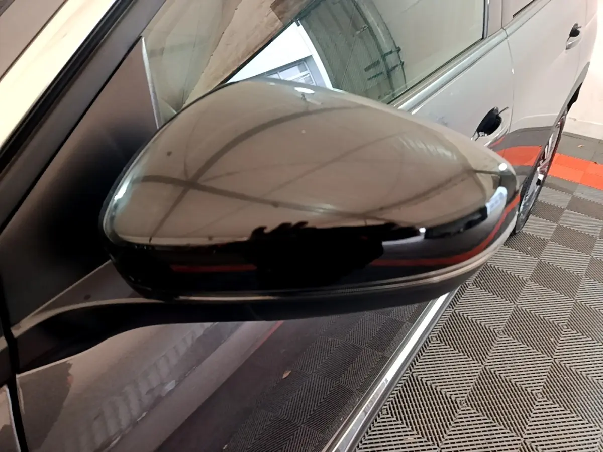 Rétroviseur droit noir brillant du Peugeot 3008 gris foncé, vue rapprochée avec reflet du plafond du garage.