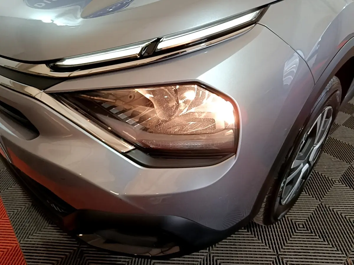 Gros plan sur le phare avant droit allumé d'une Citroën C4 gris foncé, avec partie de la roue visible.